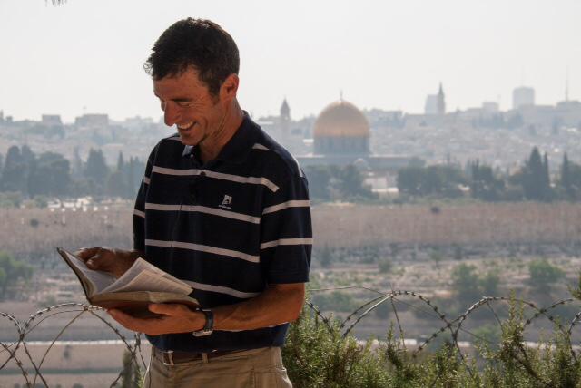 man standing with his bible open and the city of Jerusalem in the background