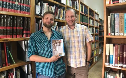 Two Caspari employees, Alec and David, in the Caspari Center library, holding a book called Facts and Myths About the Messianic Congregations in Israel