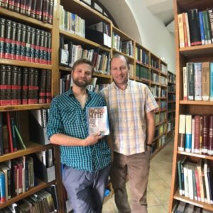 Two Caspari employees, Alec and David, in the Caspari Center library, holding a book called Facts and Myths About the Messianic Congregations in Israel