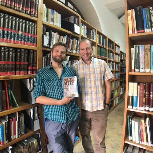 Two Caspari employees, Alec and David, in the Caspari Center library, holding a book called Facts and Myths About the Messianic Congregations in Israel